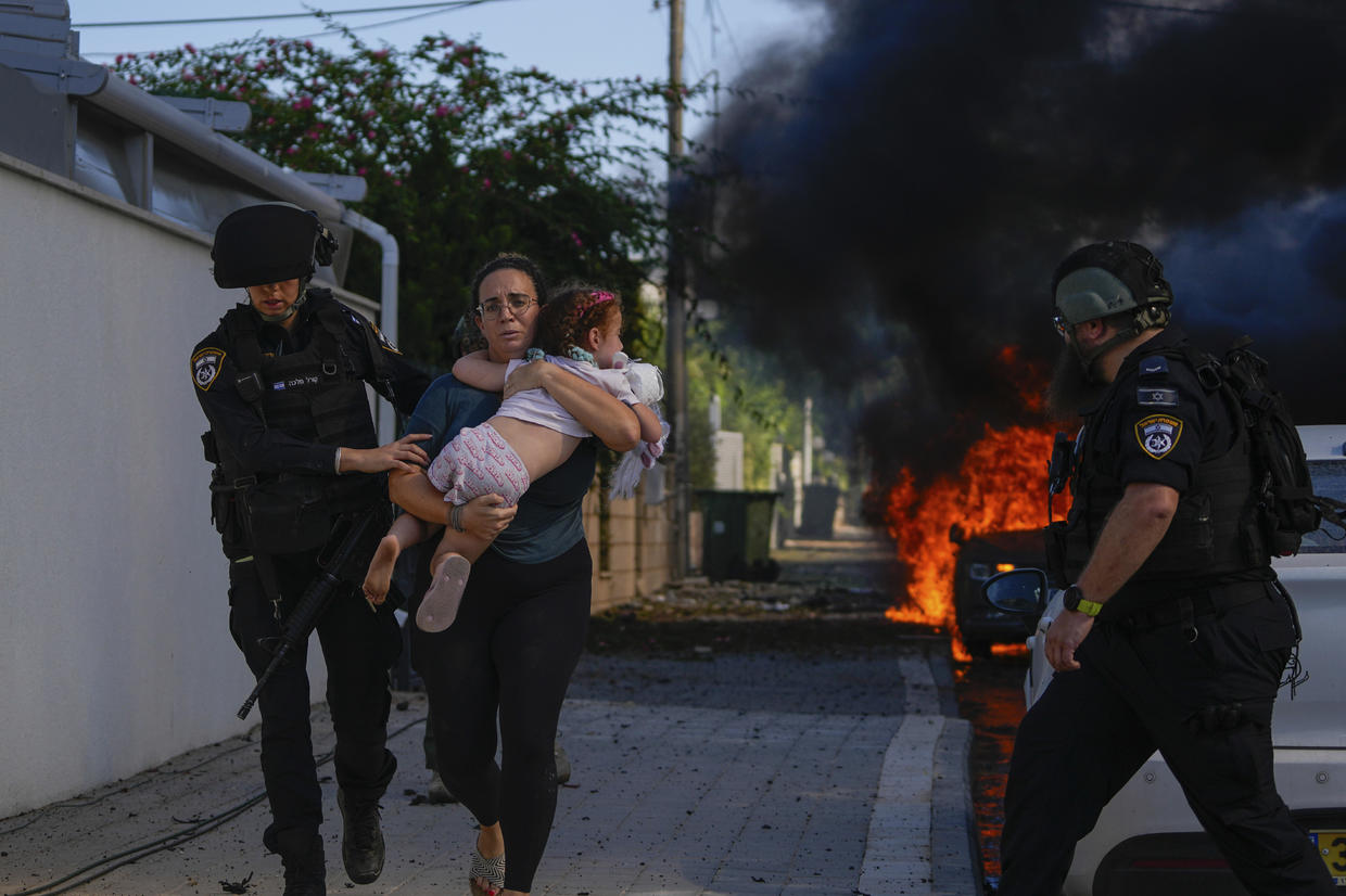 Cảnh sát Israel hỗ trợ một người phụ nữ ôm con gái chạy khỏi khu vực bị trúng tên lửa bắn từ Dải Gaza, ở Ashkelon, miền nam Israel vào ngày 7/10. Ảnh: AP